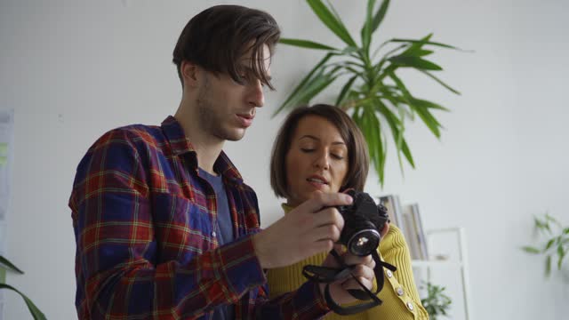 Tilt up of male photographer and female flatlay stylist taking pictures of objects arranged on table to make Christmas still life images, then checking and discussing photos on camera
