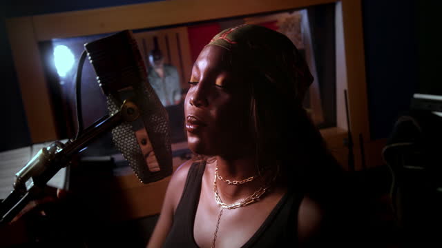 Female artist singing on microphone in music studio recording booth