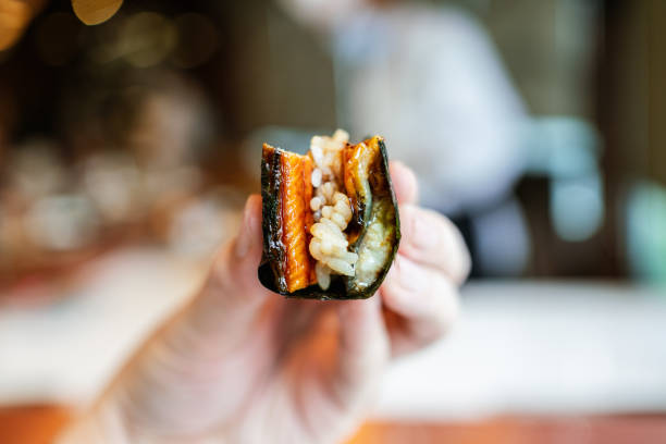 japanese omakase meal: close-up unagi (japanese grilled eel) hand roll with crispy grilled seaweed and sushi rice in hand. japanese traditional and luxury meal. - handroll imagens e fotografias de stock