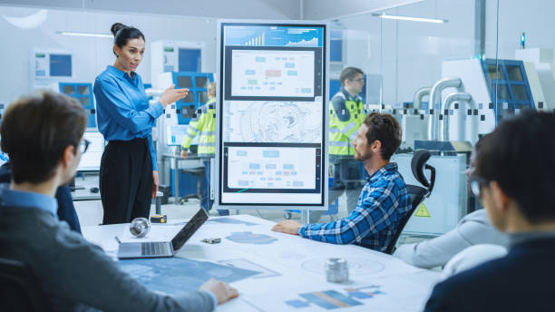 istock On a Meeting: Confident Female Engineer Talks to a Group of Specialists, Managers, Uses Interactive Digital Whiteboard to Show New Eco Friendly Engine Concept. Sustainable Green Energy Research 1282701227