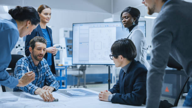 istock Busy Diverse Team of Computer Engineers and Specialists Gather Around Conference Table, They Discuss Project Drafts and Blueprints, Find Problem Solutions. Electronic Technology Factory Meeting Room 1282701255