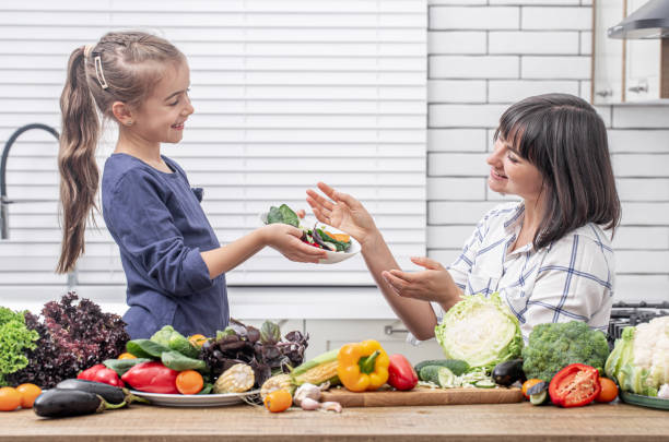 счастливые мама и дочь готовят овощной салат. концепция здорового питания. - mother green sparse contemporary стоковые фото и изображения