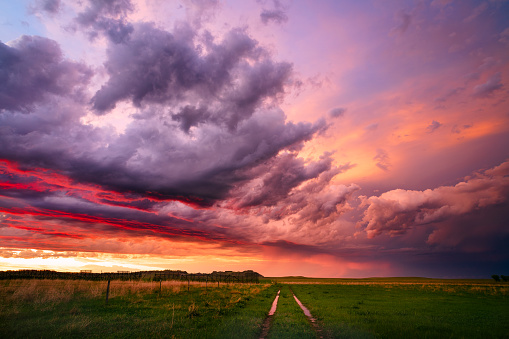 Colorful sunset sky over a dirt road and field behind a passing summer storm near Camp Crook, South Dakota.