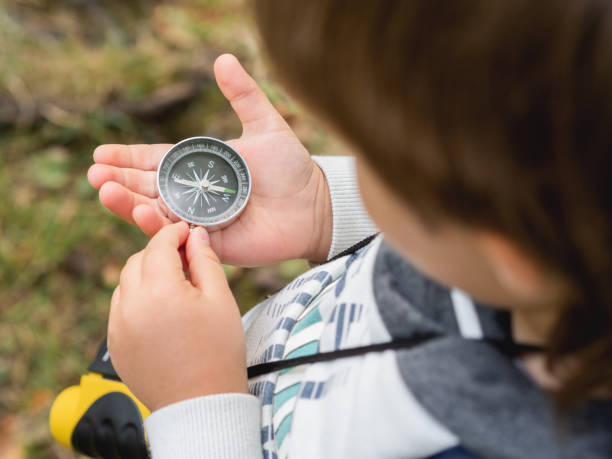 istock Little explorer on hike in forest. Boy with binoculars and compass sits on stump and reads map. Outdoor leisure activity for children. Summer journey for young tourist. 1282704647