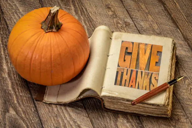 give thanks - word abstract in vintage letterpress wood type in a retro journal with pumpkin against  rustic wood, Thanksgiving concept