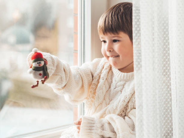 istock Kid with felt decorative snowman for Christmas tree. Boy in cable-knit oversized sweater. Cozy outfit for snuggle weather. Funny character with red Santa Claus hat. Winter holiday spirit. New year. 1282705695