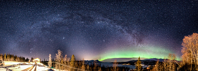 Panoramic view of Milky Way which starts in the middle of brilliant green Aurora . It is curved above horizon line and shining over mountains in Norway at winter night. Rossvatnet Lake, Hattfjelldal