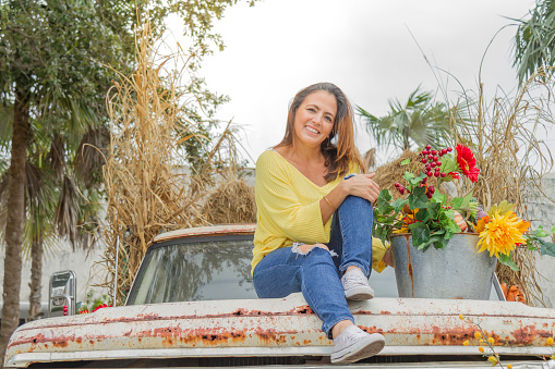 Thanksgiving Latin Experience in USA.

Happiness beautiful smiling fashion latin woman enjoying Thanksgiving Day or Halloween Season in United States, wearing a yellow shirt, blue jeans and white shoes, picking up in a cozy farm with a basket, tractor and old car: wild and sunflowers, pumpkins, vegetables on a warm cloudy autumn day.