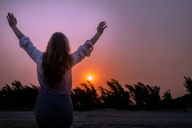 Photo of Celebrating life - Woman raises her arms at sunset