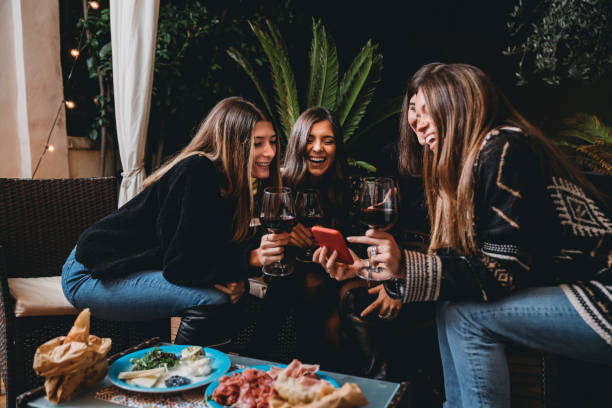 Friends drinking red wine and looking at a smartphone together Friends drinking red wine and looking at a smartphone together. They are in a patio outdoor. Four friends. friends in bar with phones stock pictures, royalty-free photos & images