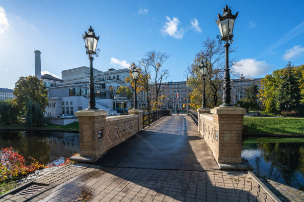 Riga, Latvia - October 24, 2020: City canal and Opera park in autumn. In the background the Latvian National Opera building can be seen. People can be seen crossing the bridge