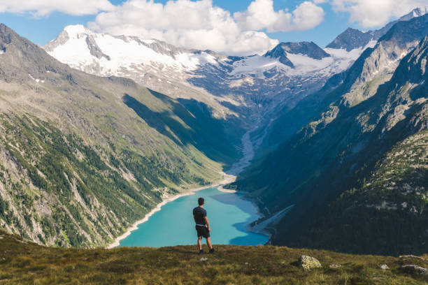 istock Young backpacker boy with the back at the camera watching a beautiful view over a lake in the Alps, scenic mountains in the background 1282719138
