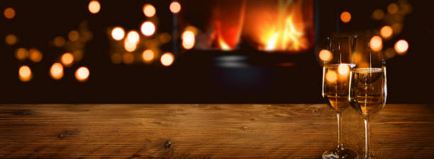 Champagne in front of a log fire Champagne on rustic wood in front of a log fire with golden bokeh lights. Horizontal background for celebrations and cozy evenings with space for your text and decorations. warming up stock pictures, royalty-free photos & images