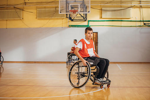 Two men, teenage male wheelchair basketball player on training indoors.
