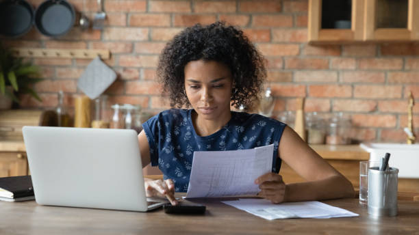 mulher biracial milenar gerencia finanças domésticas na cozinha - home finances debt tax finance - fotografias e filmes do acervo