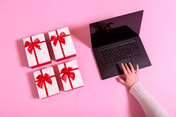 Shopping online with a notebook on a pink background Above view with a woman's hand shopping online gifts from a laptop. Electronic commerce with a notebook and gift boxes on a pink table. gift lounge stock pictures, royalty-free photos & images