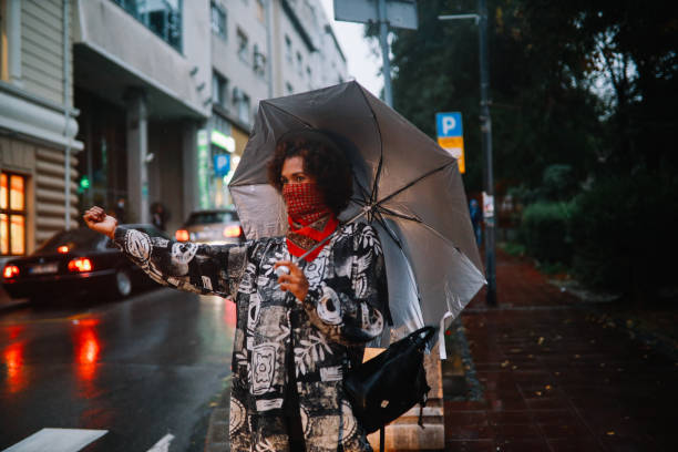 donna nera che sventola per un taxi, indossando una maschera di andatura del collo - candid women african descent umbrella foto e immagini stock