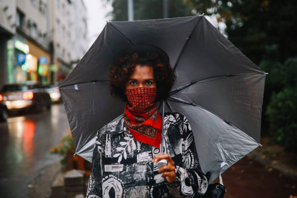 donna nera che indossa un'andatura del collo invece della maschera protettiva per il viso - candid women african descent umbrella foto e immagini stock