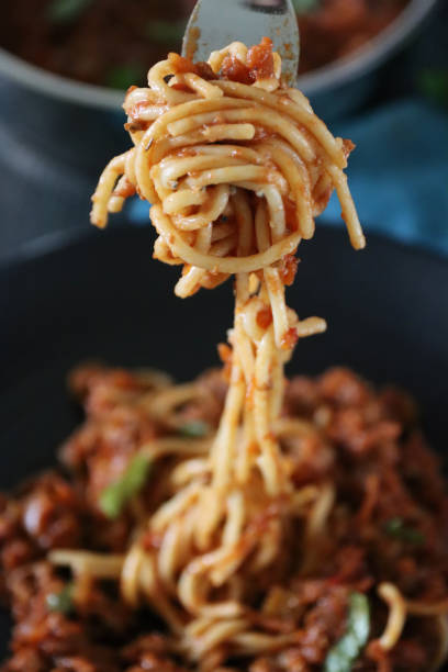 image of metal fork twirling spaghetti pasta topped with homemade bolognese sauce of lean beef mince, rich tomato sauce, onions, garlic and basil leaf garnish, portion on black plate, elevated view, focus on foreground - spaghetti cooked heap studio shot imagens e fotografias de stock