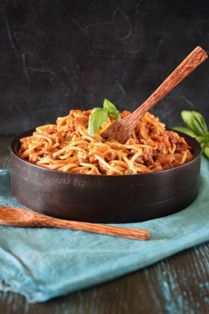 image of spaghetti pasta mixed with homemade bolognese sauce of lean beef mince, rich tomato sauce, onions, garlic and basil leaf garnish in black bowl with wooden serving utensils, focus on foreground - spaghetti cooked heap studio shot imagens e fotografias de stock