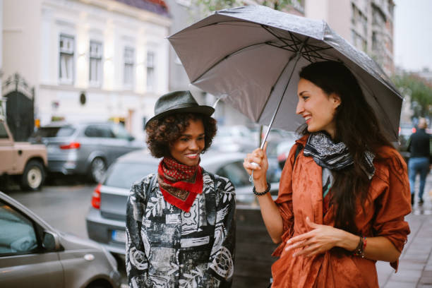 amici per strada che indossano bandane invece di maschere per il viso per uso interno - candid women african descent umbrella foto e immagini stock