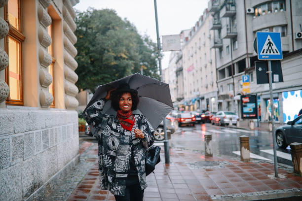 giovane donna che cammina in una giornata piovosa - candid women african descent umbrella foto e immagini stock