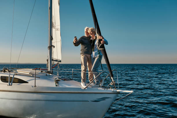 Happy moments. Full length of beautiful senior couple making selfie on smartphone and smiling while standing together on the side of sailboat or yacht deck floating in sea Happy moments. Full length of beautiful senior couple making selfie on smartphone and smiling while standing together on the side of sailboat or yacht deck floating in sea. Boat trip, travelling yacht selfie stock pictures, royalty-free photos & images