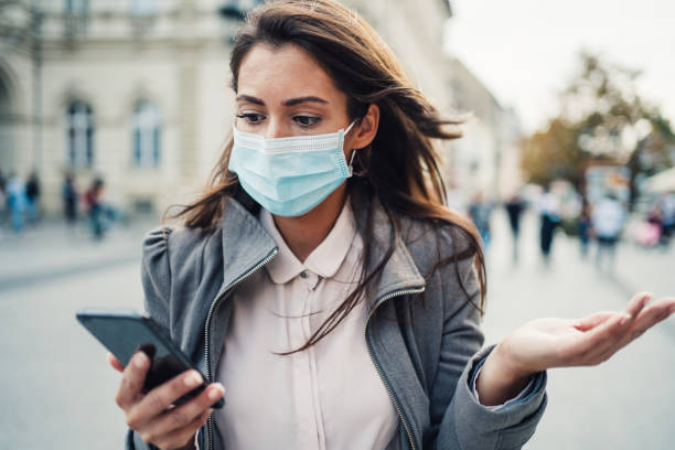 istock Woman with protective face mask using smart phone outdoors. 1282729696
