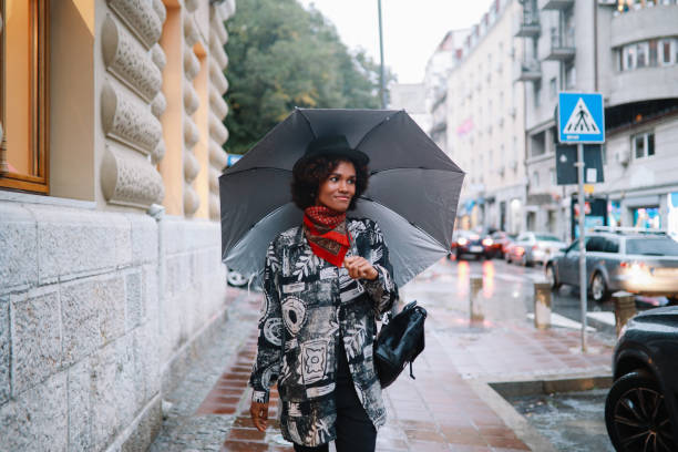 giovane donna che cammina in una giornata piovosa - candid women african descent umbrella foto e immagini stock