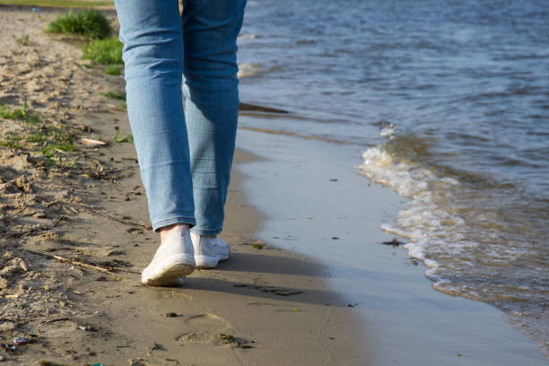 piernas de una chica caminando a lo largo de la orilla del río - child human foot barefoot jeans fotografías e imágenes de stock