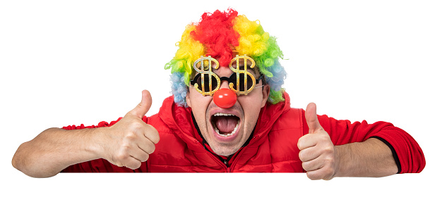 Funny clown in a multi colored wig with his thumbs up leaning over a white blank sign. He is wearing golden dollar shaped sunglasses. Isolated on white. You can add extra white space with your message to the bottom.