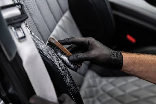 Car detailing studio worker cleaning car interior and car leather seats with a brush. stock photo