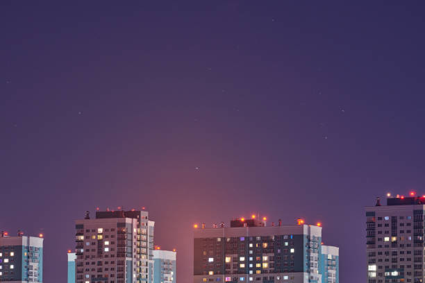 Multistorey buildings at night lights, copy space. Long exposure photography, stars tracks in purple sky. Multi-storey high rise residential skyscrapers for rent apartment in urban city.