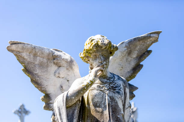 istock Angel, old statue of angle with finger on lips, light blue sky background with copy space 1282735378