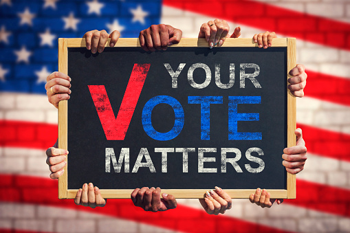 A lot of hand are holding a banner with text YOUR VOTE MATTERS on background of American flag. Your Vote Matters. Concept of voter rights and US election.