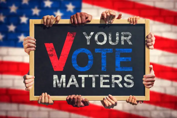 Photo of A lot of hand are holding a banner with text YOUR VOTE MATTERS on background of American flag. Your Vote Matters. Concept of voter rights and US election.