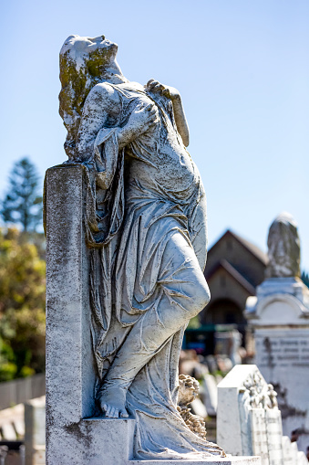 Old statue of grieving young woman in Waverley cemetery build in 1877, the artist is unknown Sydney Australia, looking up, background with copy space, vertical composition