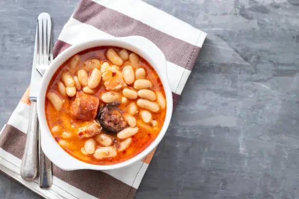 Photo of typical spanish dish fabada, beands with smoked sausages and meat on bowl