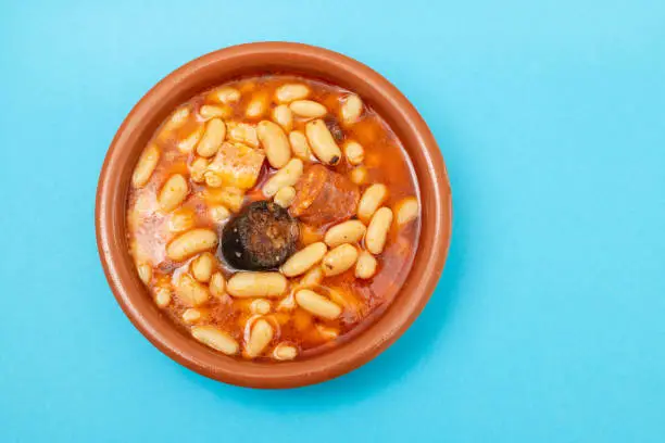Photo of typical spanish dish fabada, beands with smoked sausages and meat on brown ceramic dish