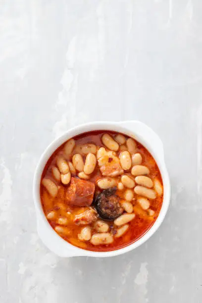 Photo of typical spanish dish fabada, beands with smoked sausages and meat on white dish
