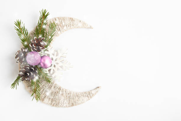 Photo of Snowy fir tree branch, pink balls and pine cones on white crescent and snowflake. Top view with copy space. Flat lay. Christmas background or postcard. New year concept
