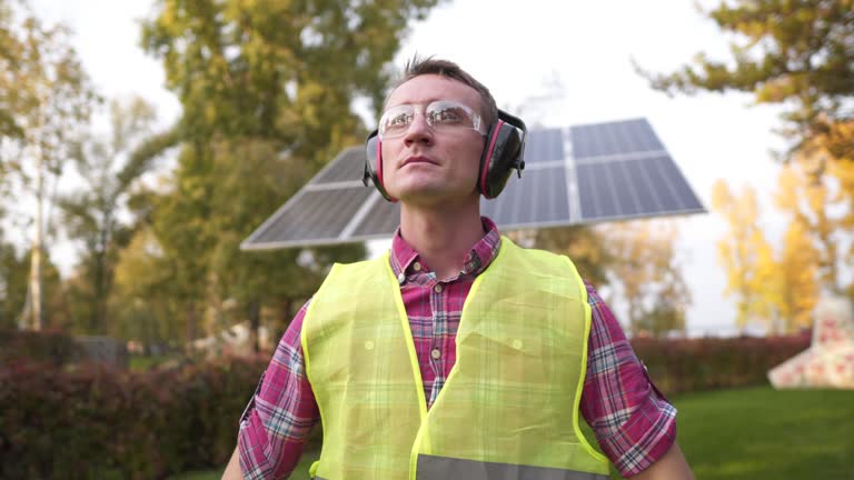 An engineer with headphones works at solar station. Worker puts on earphones for sound protection near solar panel . Caring for health, safety at work. Earplugs. Too loud sound, hearing impairment.