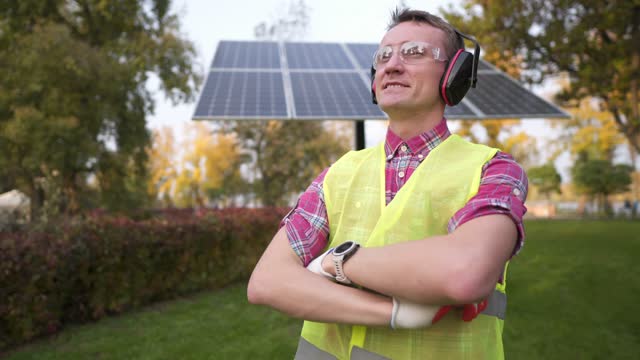 Man wearing hearing protection safety equipment at solar power station. Engineer wears noise canceling headphones or earphones against of solar panel. Foreman puts on protective ears with headphones.