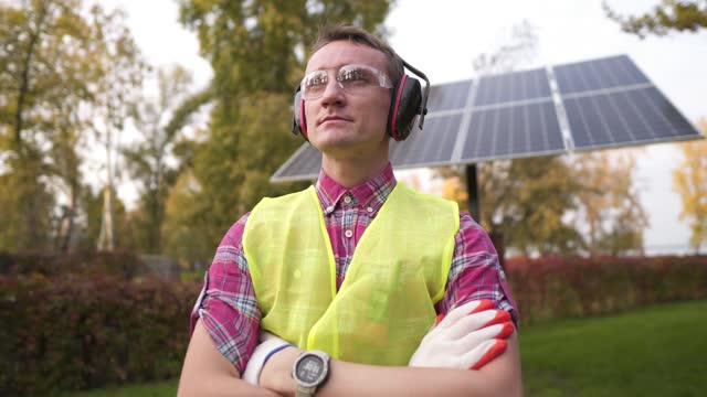 Technician or engineer with protective headphones standing near the solar panel. Man wearing safety equipment hearing protection. Worker wearing noise cancelling ear defenders or ear muffs.