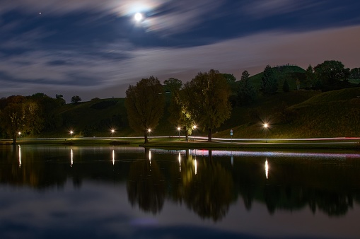 Long exposure of city lights and clouds in a park by night. Long exposure of light reflections in a lake in Munich at night.