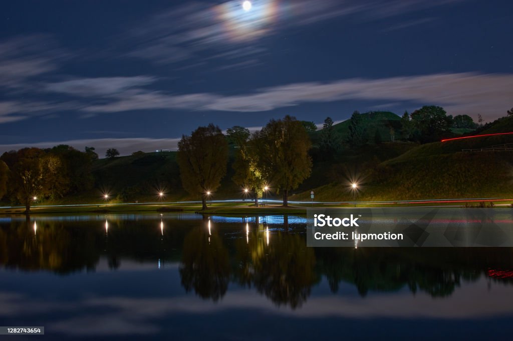 Long exposure of city lights and clouds in a park by night. Long exposure of light reflections in a lake in Munich at night. Bavaria Stock Photo