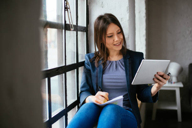 istock Happy woman sitting by the window and using digital tablet 1282743711