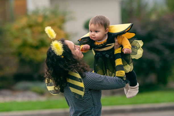 Mom and baby daughter in matching bumblebee Halloween costumes A beautiful mixed race mother holds her baby daughter up in the air while out trick or treating. The pair are dressed in matching bumblebee Halloween costumes. bee costume stock pictures, royalty-free photos & images
