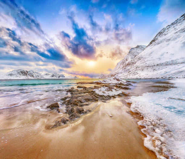 Scenic view out of the boat of beautiful snowcapped mountains and the seashore during bright sunrise on Lofoten Islands, Norway, Scandinavia