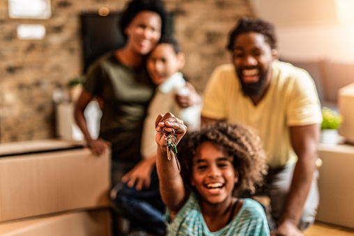 Happy African American family just moved in their new home. Girl holding home keys.